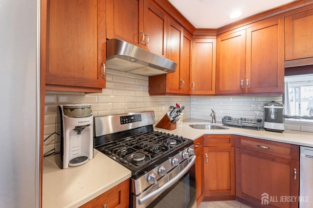 kitchen featuring backsplash, under cabinet range hood, light countertops, appliances with stainless steel finishes, and a sink