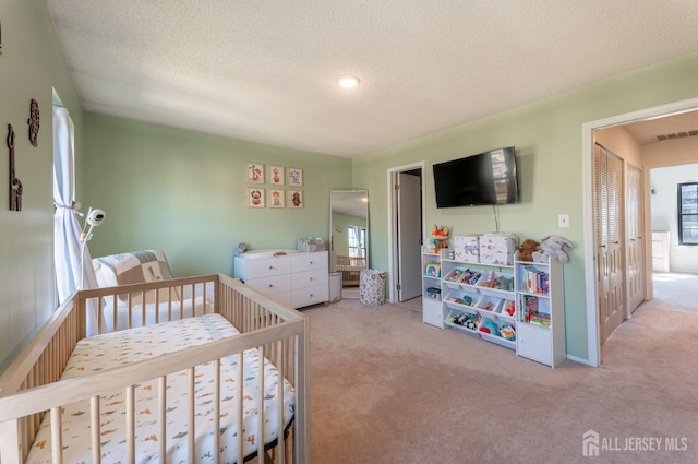 bedroom with a nursery area, carpet flooring, visible vents, and a textured ceiling