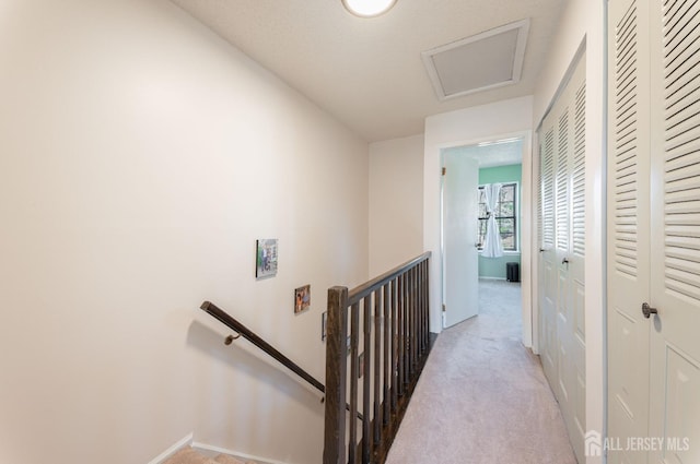 corridor with baseboards, an upstairs landing, attic access, and carpet flooring