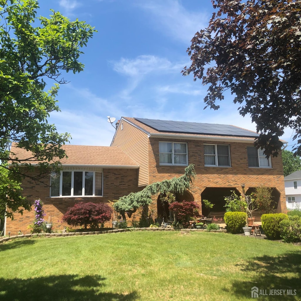 tri-level home with brick siding, solar panels, and a front lawn