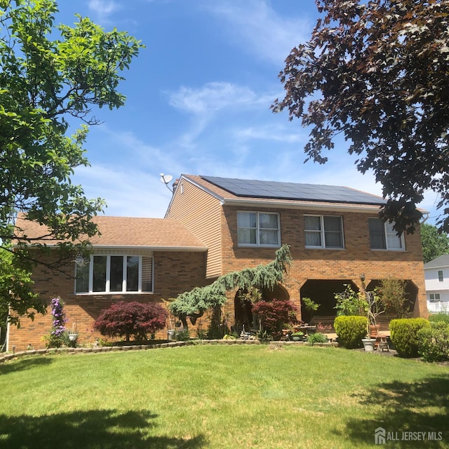 tri-level home with brick siding, solar panels, and a front lawn