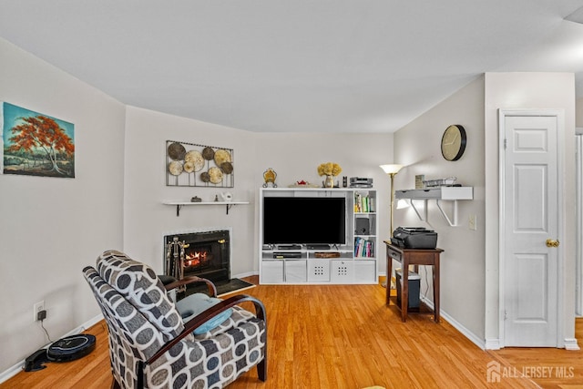 living room with a fireplace with flush hearth, baseboards, and wood finished floors