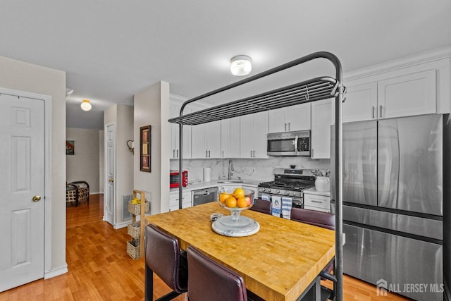 kitchen with a sink, white cabinets, light countertops, appliances with stainless steel finishes, and light wood-type flooring