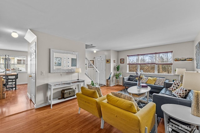 living room featuring light wood-style flooring, baseboards, and stairs