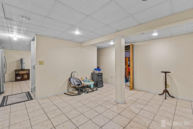 finished basement featuring light tile patterned floors, a paneled ceiling, freestanding refrigerator, and baseboards