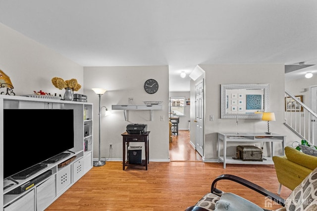 living room with light wood finished floors, baseboards, and stairway