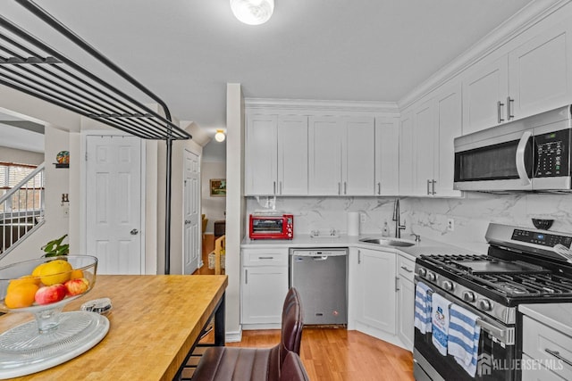 kitchen featuring stainless steel appliances, light countertops, light wood-style floors, white cabinetry, and a sink