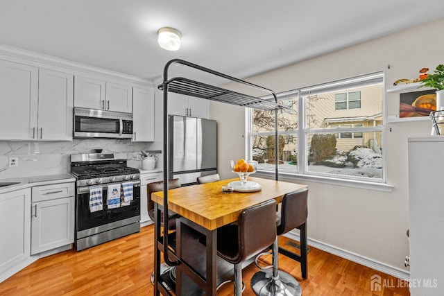 kitchen featuring decorative backsplash, light wood-style flooring, appliances with stainless steel finishes, light countertops, and white cabinetry