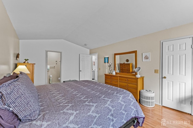 bedroom with lofted ceiling, ensuite bath, and wood finished floors