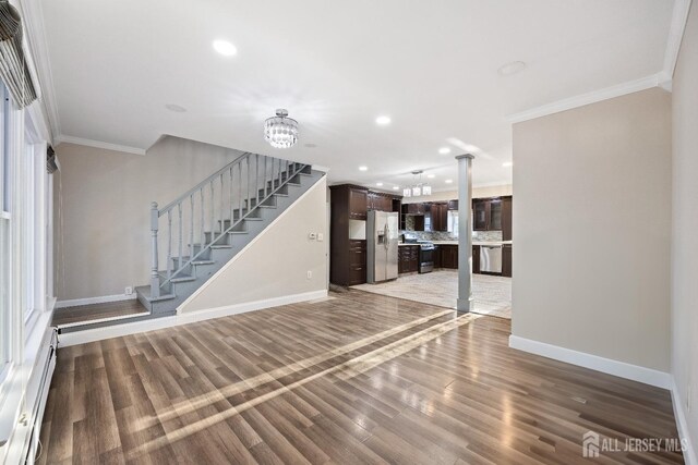 unfurnished living room featuring a notable chandelier, a baseboard heating unit, dark wood-type flooring, and crown molding