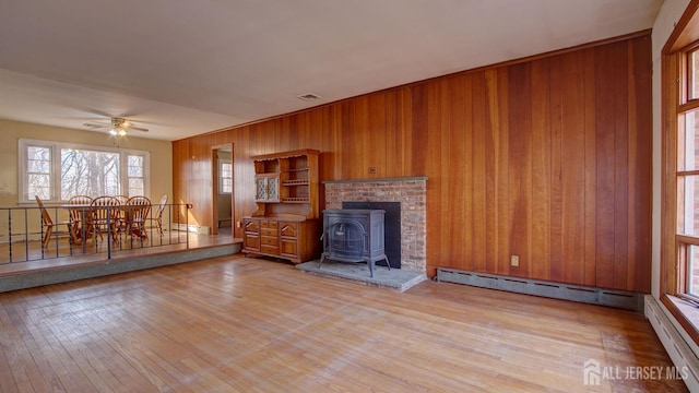 unfurnished living room with baseboard heating, a wood stove, and wood-type flooring