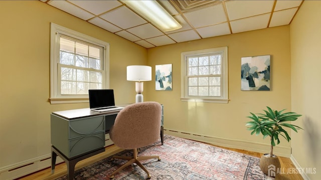 home office featuring a drop ceiling, a baseboard radiator, baseboards, and wood finished floors