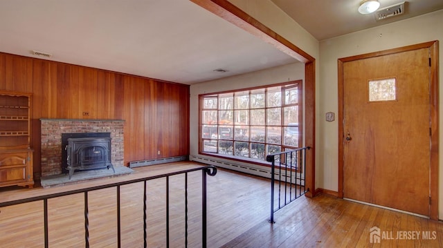 entrance foyer featuring light wood-type flooring, visible vents, wood walls, and a wood stove