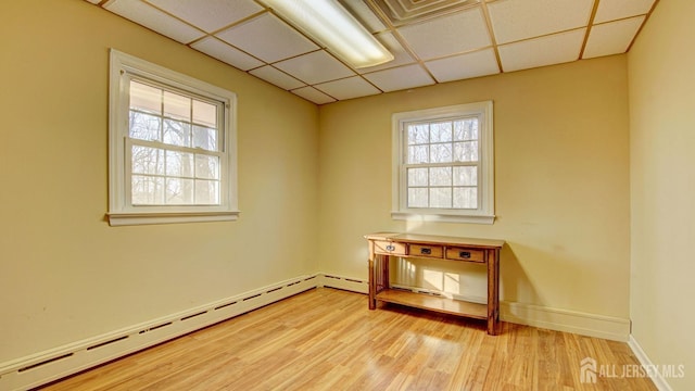 empty room with a drop ceiling, light wood-type flooring, baseboards, and baseboard heating