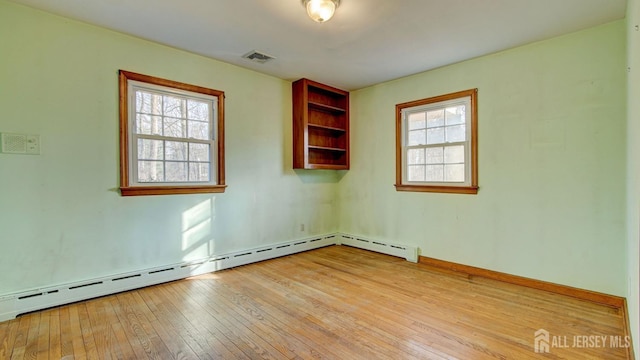 spare room featuring a baseboard heating unit, visible vents, and wood-type flooring