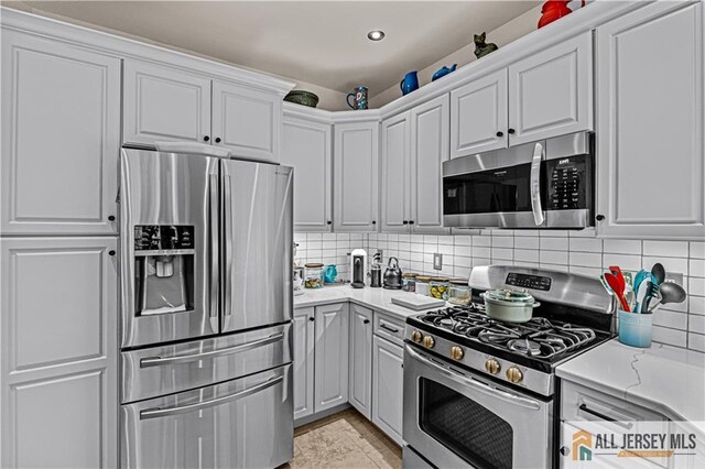 kitchen with stainless steel appliances, backsplash, white cabinets, light stone countertops, and recessed lighting