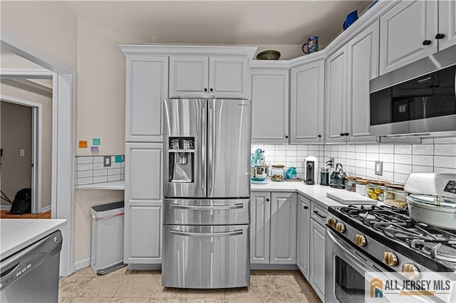 kitchen with stainless steel appliances, decorative backsplash, gray cabinetry, and light stone countertops