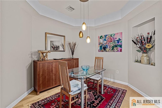 dining space featuring light wood finished floors, baseboards, and a tray ceiling