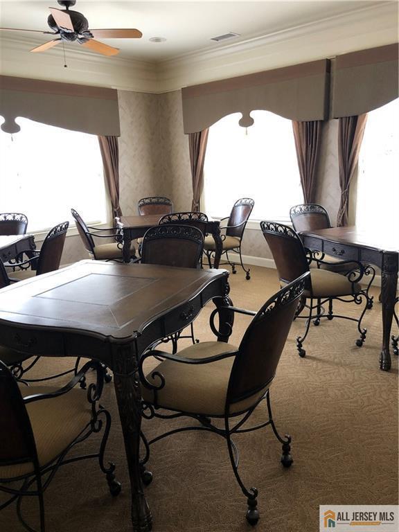 carpeted dining space with crown molding and ceiling fan