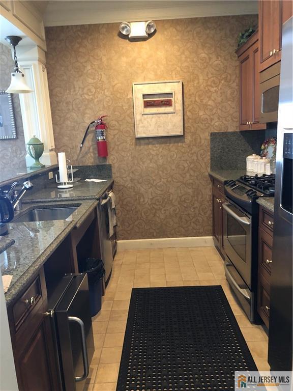 kitchen featuring stainless steel appliances, a sink, wallpapered walls, dark stone countertops, and baseboards