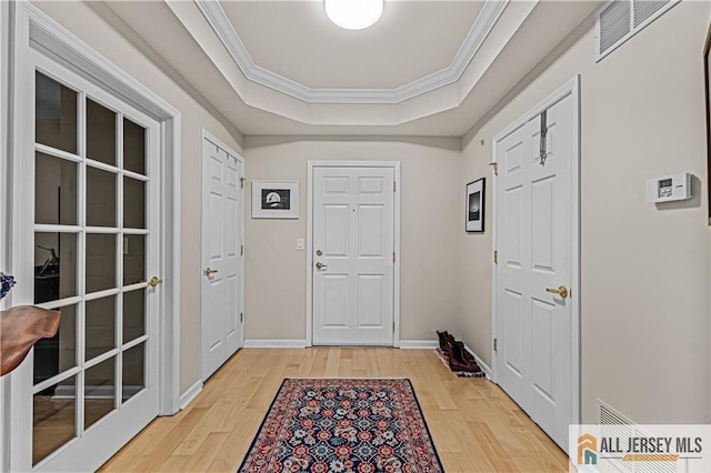 foyer entrance featuring a raised ceiling, light wood-style floors, crown molding, and baseboards