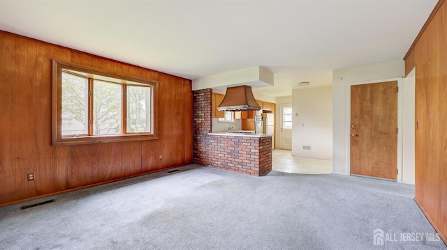 unfurnished living room with wood walls and light colored carpet