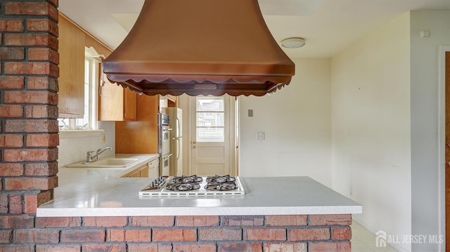 kitchen with custom range hood, a sink, gas stovetop, light countertops, and freestanding refrigerator