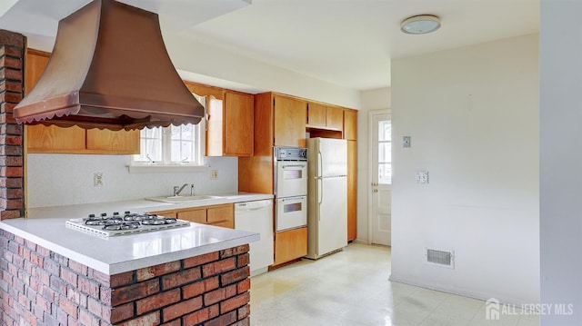 kitchen featuring custom range hood, white appliances, light countertops, a sink, and light flooring