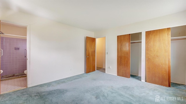 unfurnished bedroom with two closets, ensuite bathroom, and carpet flooring
