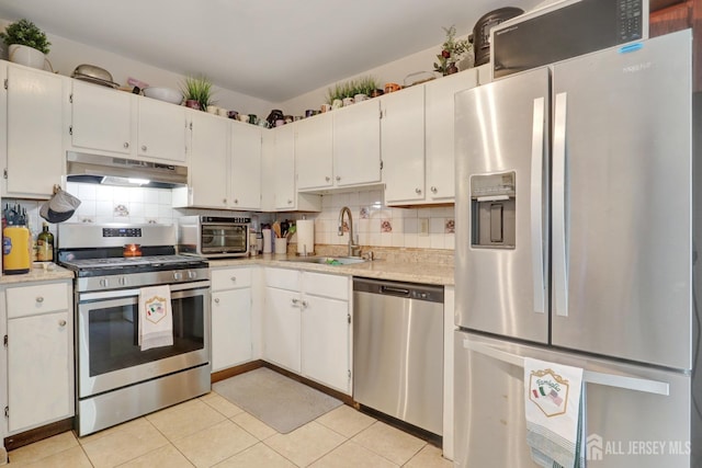 kitchen with appliances with stainless steel finishes, under cabinet range hood, a sink, light countertops, and tasteful backsplash