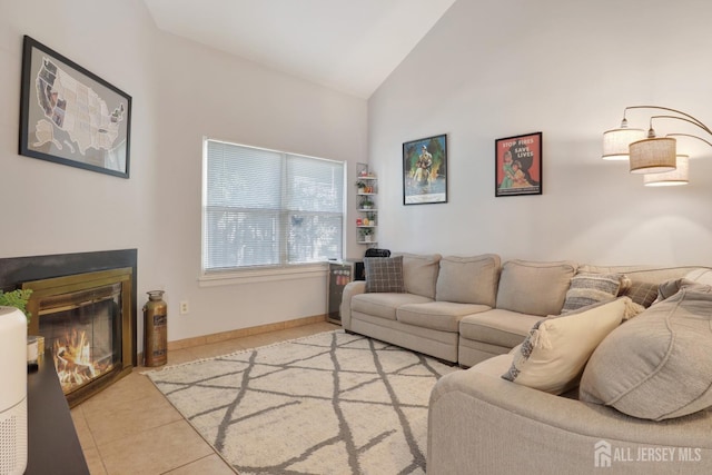 living area with a glass covered fireplace, light tile patterned floors, high vaulted ceiling, and baseboards