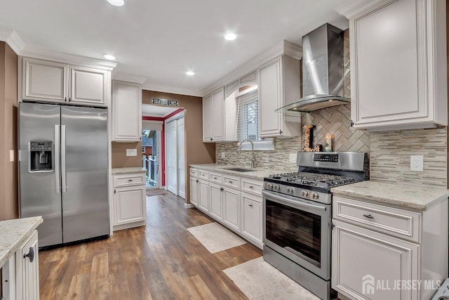 kitchen featuring appliances with stainless steel finishes, wall chimney exhaust hood, a sink, wood finished floors, and backsplash