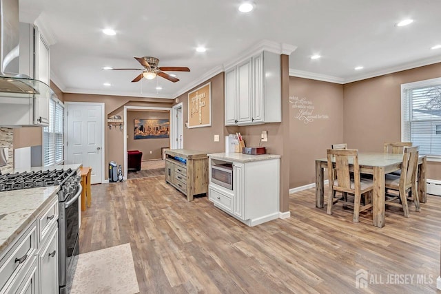 kitchen with appliances with stainless steel finishes, ornamental molding, a ceiling fan, wall chimney exhaust hood, and light wood-style floors