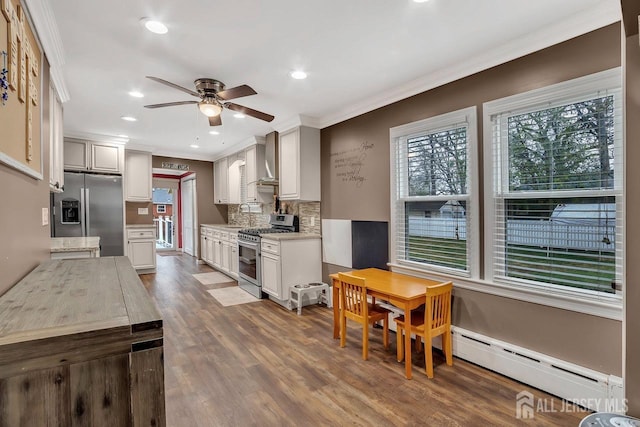 kitchen with stainless steel appliances, wall chimney exhaust hood, a ceiling fan, healthy amount of natural light, and ornamental molding