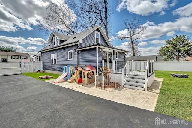 rear view of property featuring a deck, a patio area, a shingled roof, and a gate