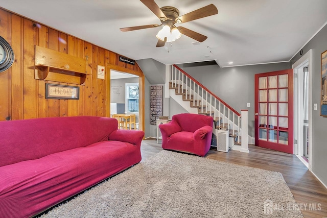 living area with stairs, ceiling fan, wood finished floors, wood walls, and baseboards