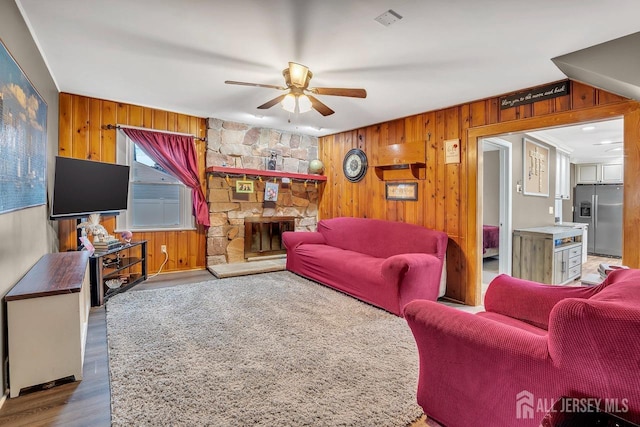 living area featuring a ceiling fan, wood walls, wood finished floors, and a fireplace
