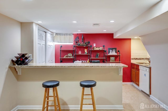 kitchen featuring a breakfast bar area, visible vents, dishwasher, a sink, and light stone counters