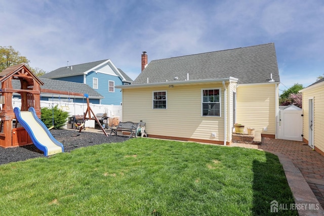 back of property with fence, a chimney, a shingled roof, a playground, and a yard