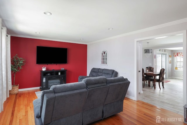 living room with ornamental molding, a glass covered fireplace, baseboards, recessed lighting, and light wood-style flooring
