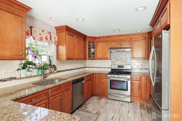 kitchen featuring under cabinet range hood, brown cabinets, appliances with stainless steel finishes, and a sink