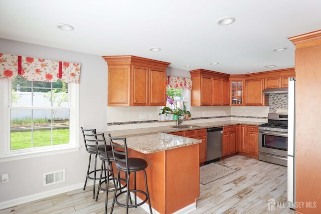 kitchen featuring appliances with stainless steel finishes, brown cabinetry, a peninsula, and visible vents