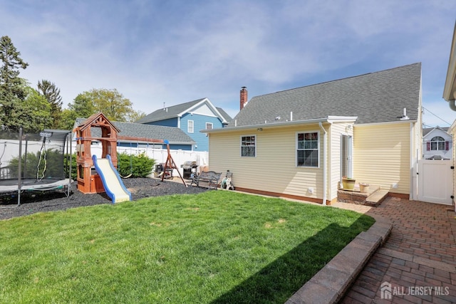 back of property with fence, a trampoline, a patio area, a playground, and a lawn