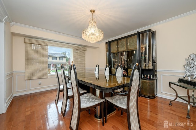 dining space featuring ornamental molding, a chandelier, wood finished floors, a decorative wall, and wainscoting