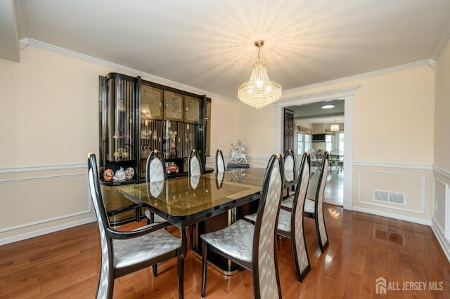 dining area with a chandelier, crown molding, wood finished floors, a decorative wall, and a wainscoted wall