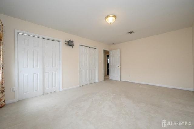 unfurnished bedroom featuring multiple closets, baseboards, and light carpet