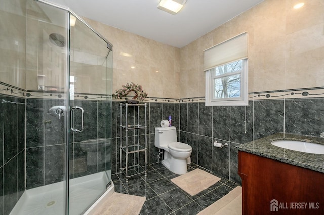 bathroom featuring tile walls, toilet, vanity, a stall shower, and tile patterned flooring
