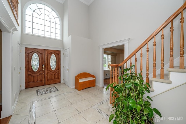 foyer with a towering ceiling, baseboards, stairs, inlaid floor details, and light tile patterned floors