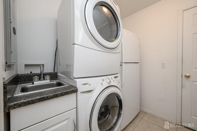 clothes washing area with stacked washing machine and dryer, light tile patterned flooring, and cabinet space