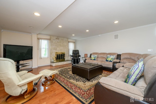 living room with wood finished floors, crown molding, recessed lighting, a stone fireplace, and baseboards